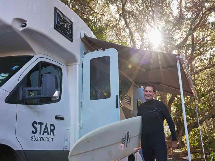 Man with surfboard outside motorhome